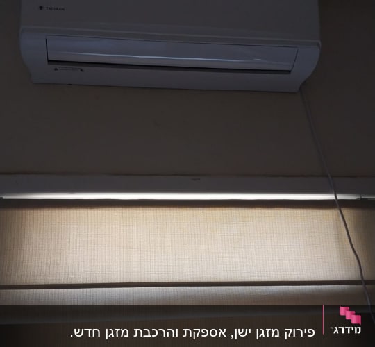 מזגן קיר לבן מותקן מעל חלון עם וילון